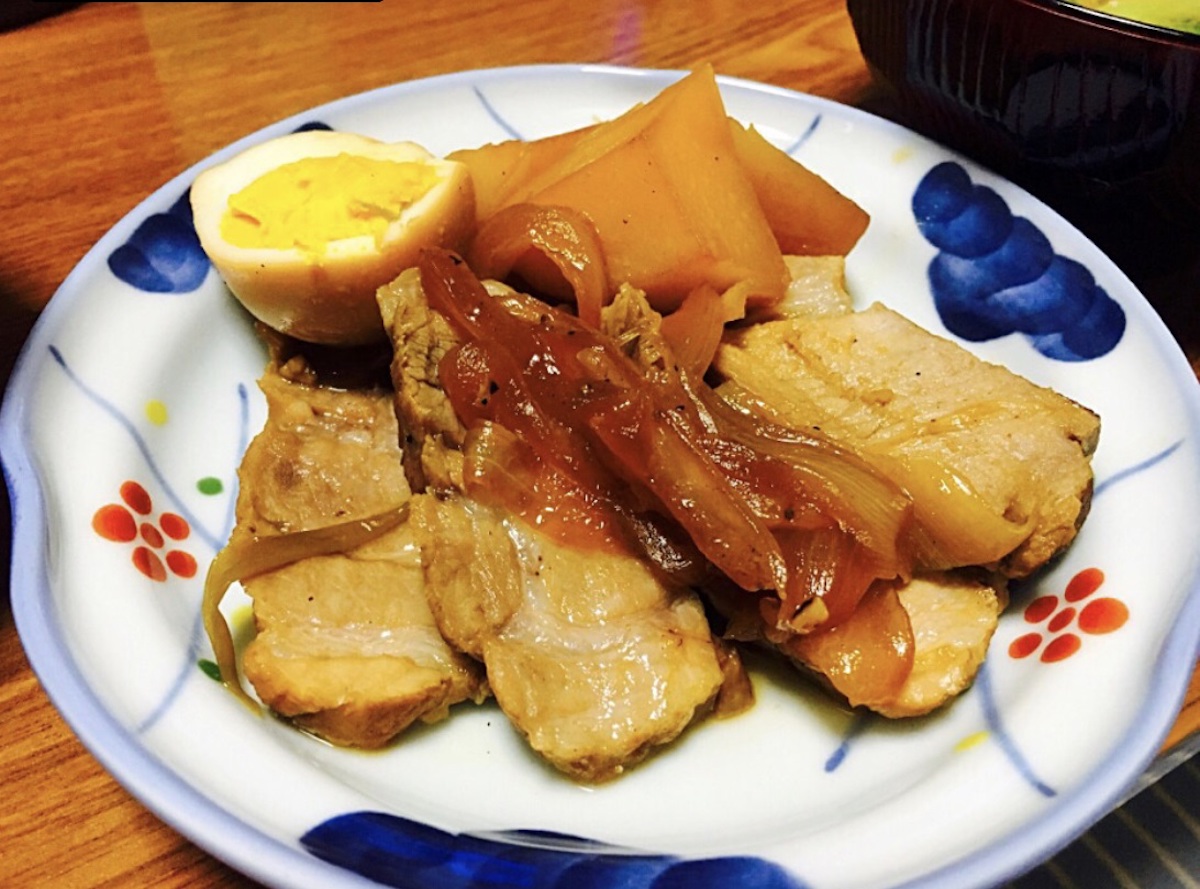 Grilled pork loin, onion and hard boiled egg is on a plate.