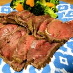 10 pieces of sliced roast beef with cooked broccoli and carrots on a blue plate.