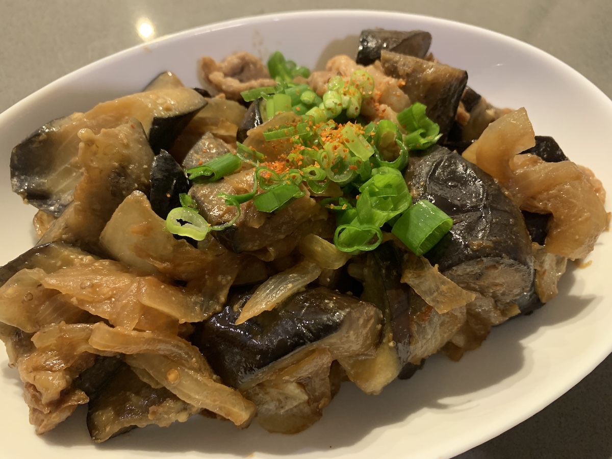 Stir fried eggplants and pork are on a white plate.